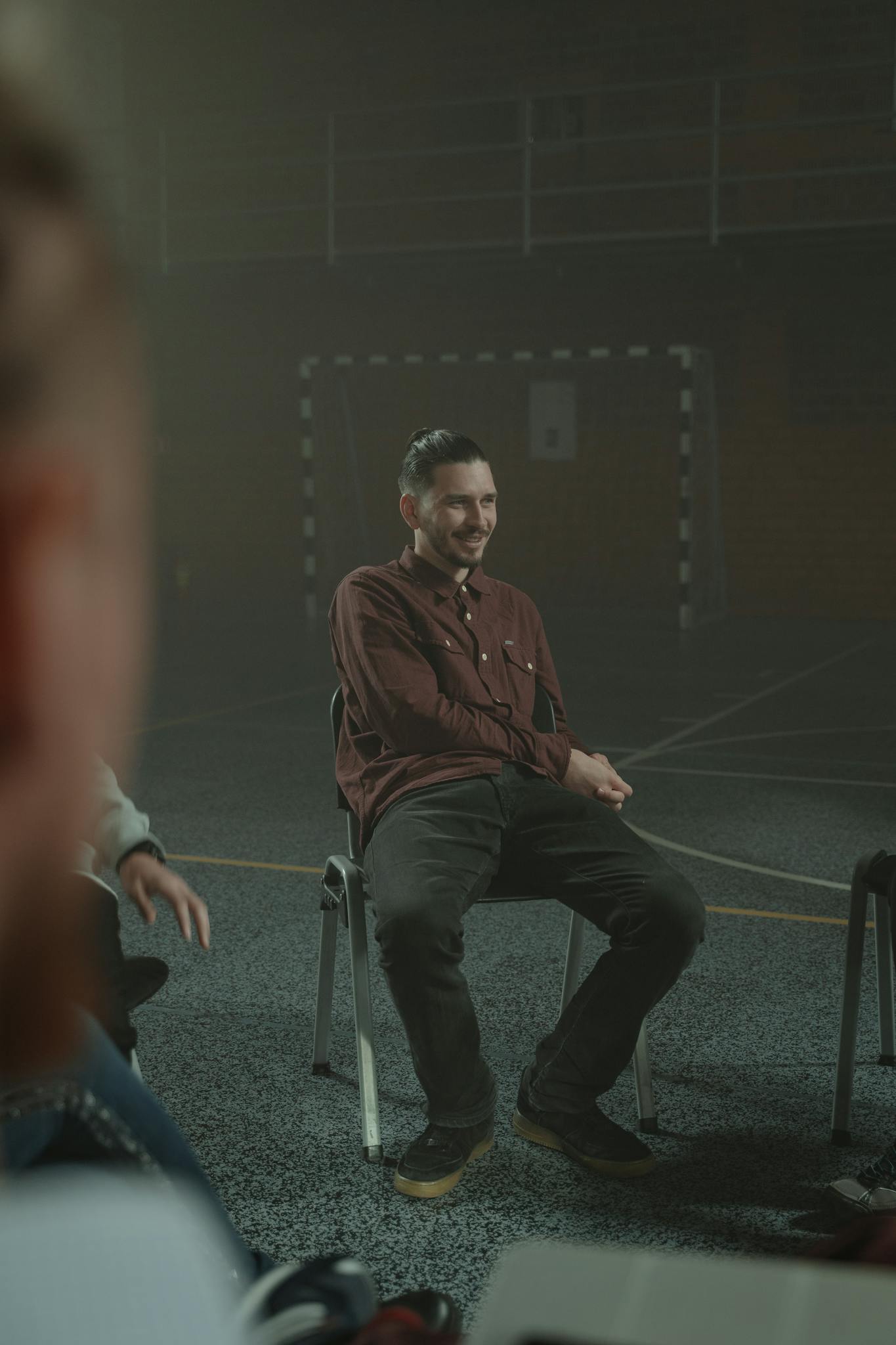 Adults engaged in a group therapy session inside a dimly lit, smoky room.